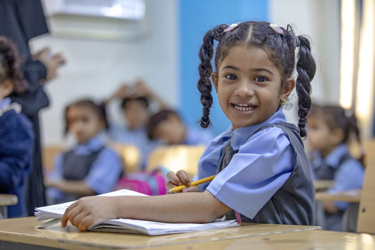 A young girl smiles from her desk