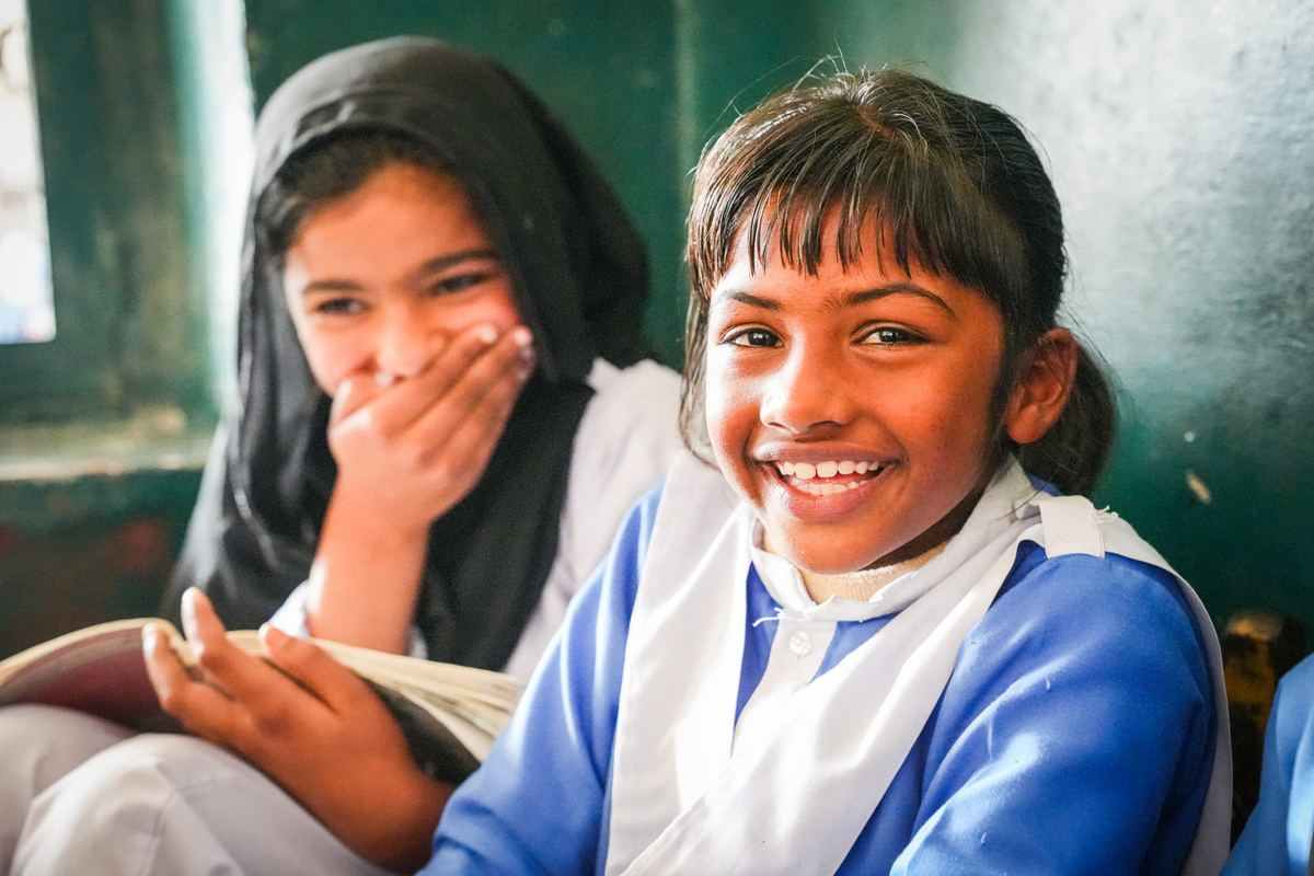 Two schoolgirls laugh together in class