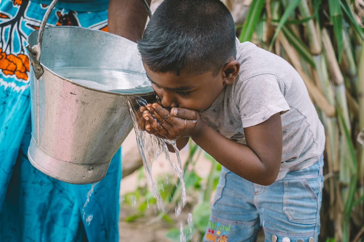 A boy drinks clean water poured from a metal bucket