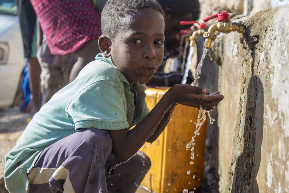 A boy cups his hands under a flowing tap