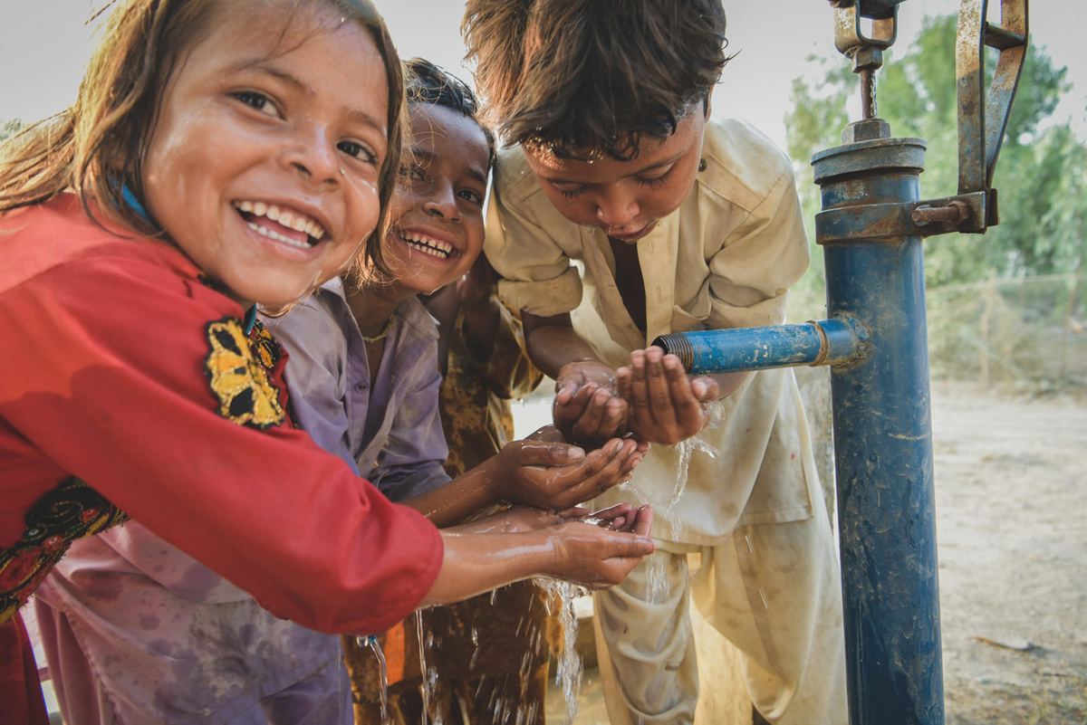 Children laughing as they drink from a tap