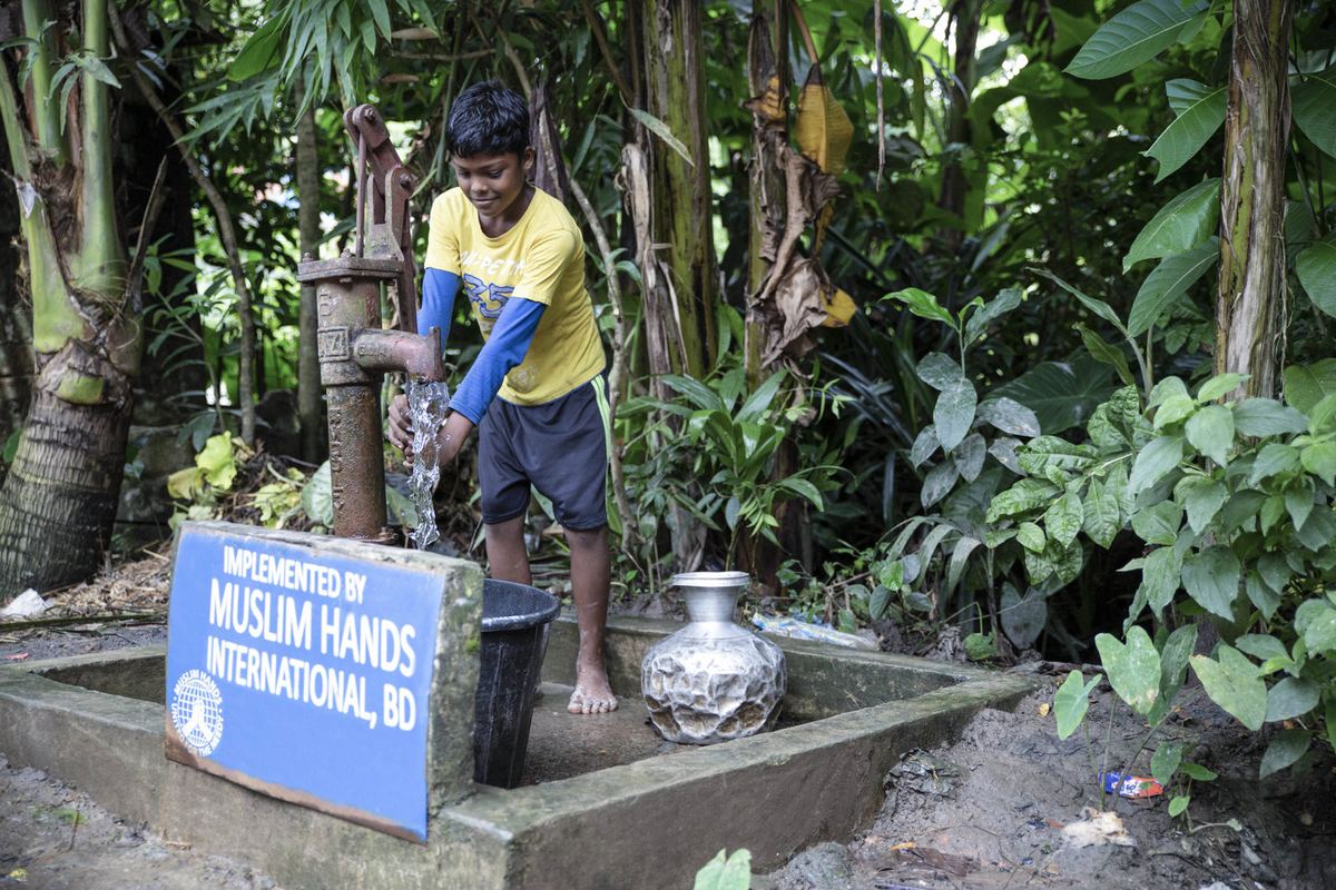 A boy uses a hand pump beside a Muslim Hands sign