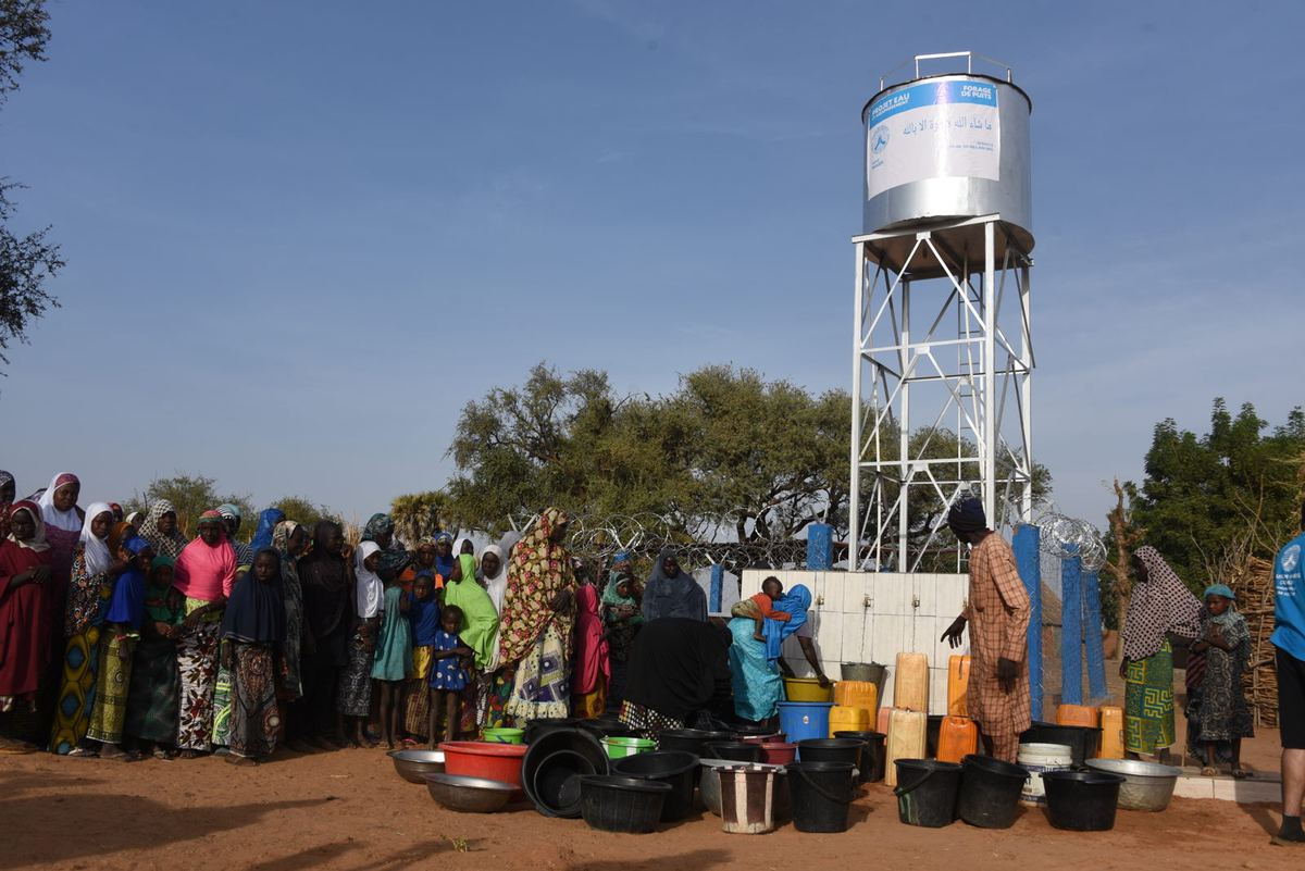 A community gathers with containers at a water tower